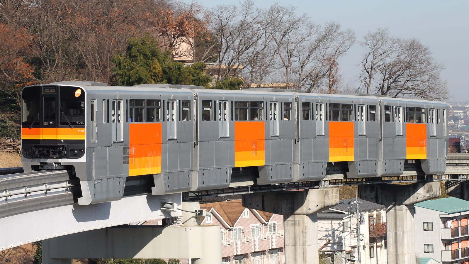 An orange-striped Tama Monorail train arriving at Tama-Dobutsukoen Station