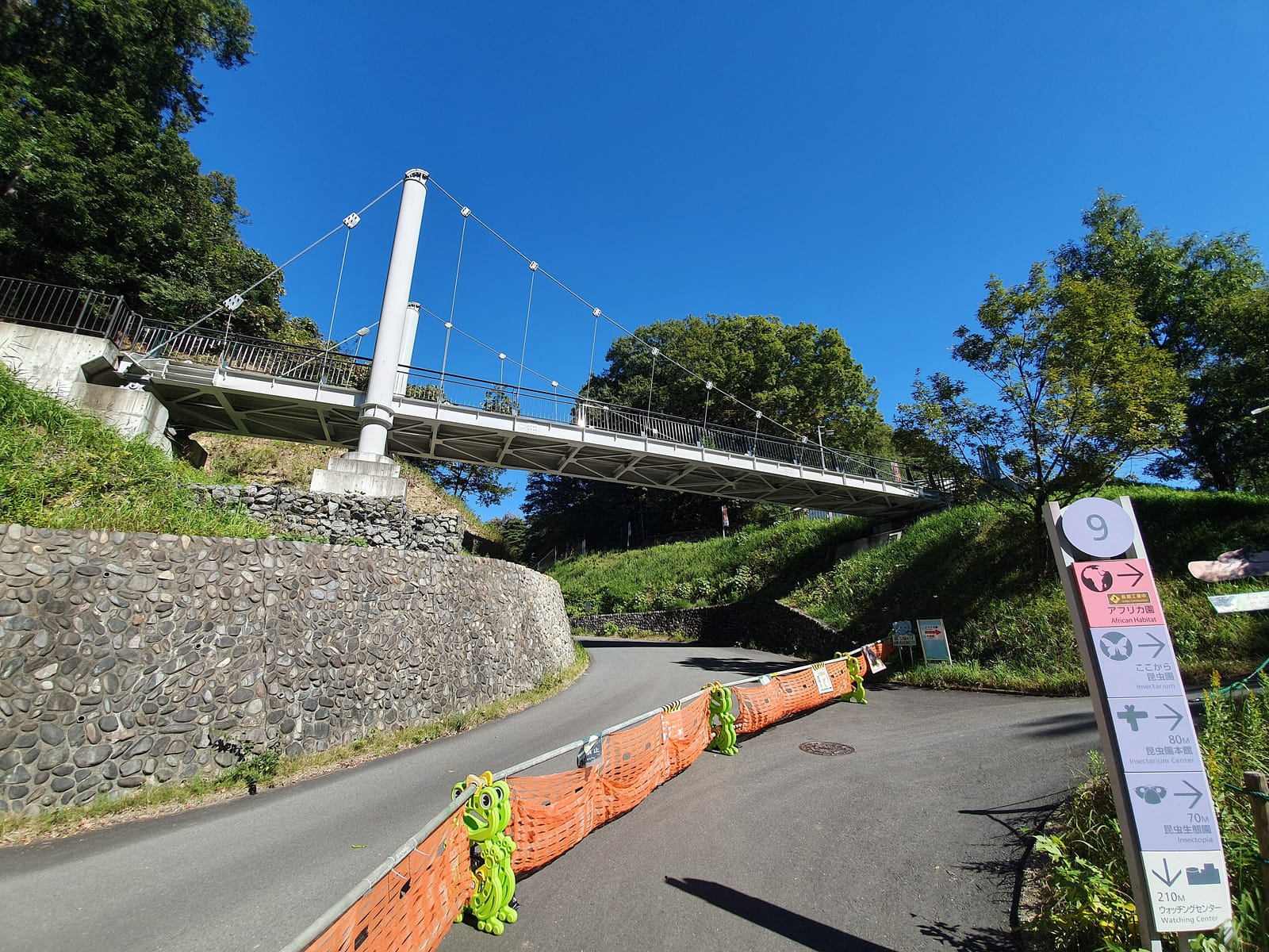 A steep paved path climbing under a footbridge inside Tama Zoo, with a direction signpost