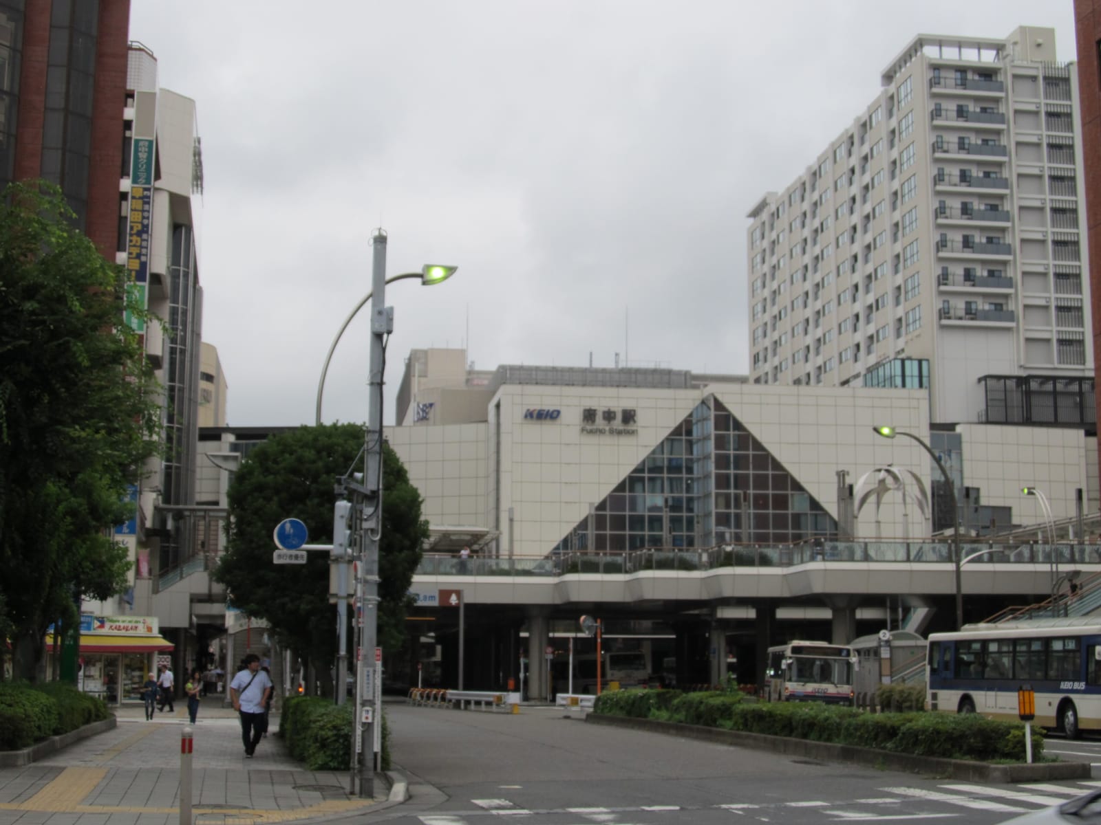 The Keio Fuchu Station building with its glass triangle facade, seen from the street outside.