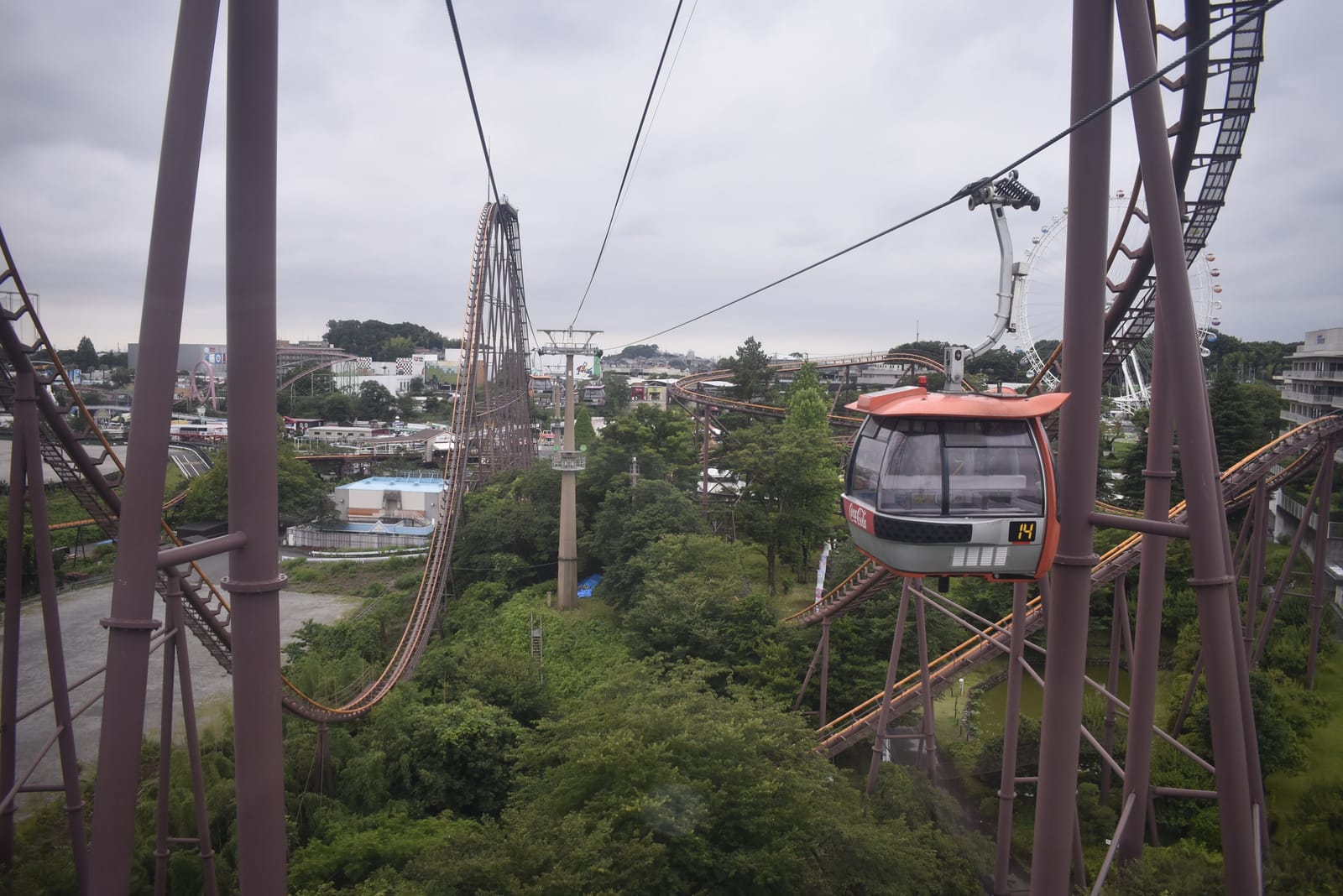 View from a Sky Shuttle cabin over green slopes and Yomiuriland's roller coaster tracks, with another cabin passing.