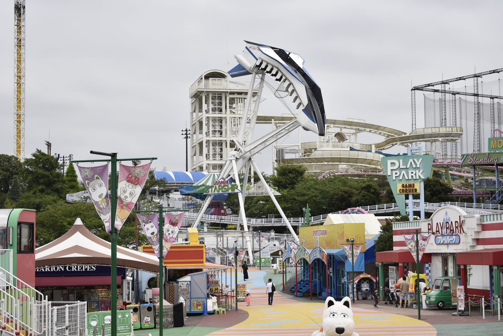The Starship swinging ride rising above a colourful main path lined with food stands at Yomiuriland.