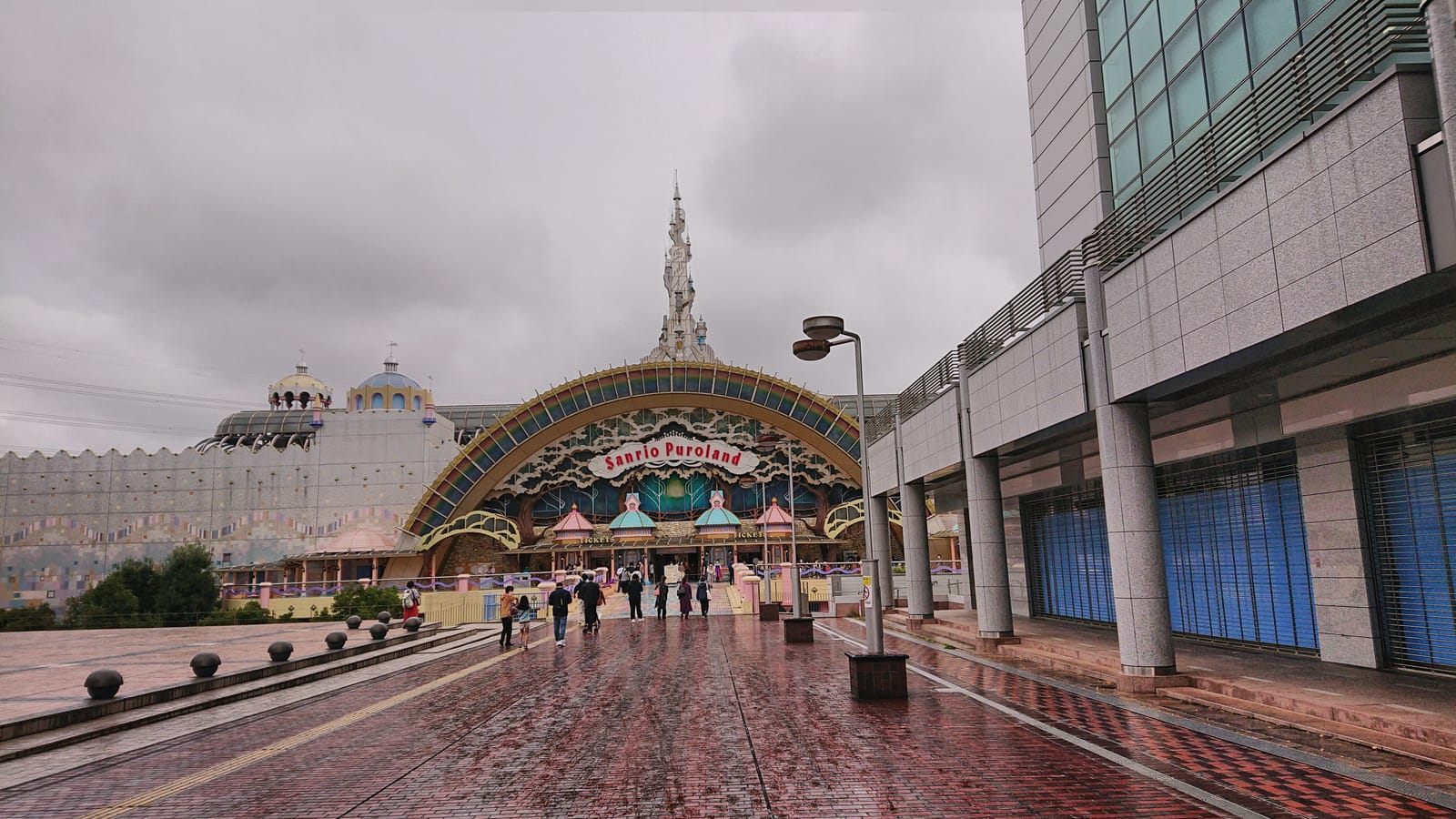 The wide brick promenade leading to Sanrio Puroland's arched entrance on a cloudy day