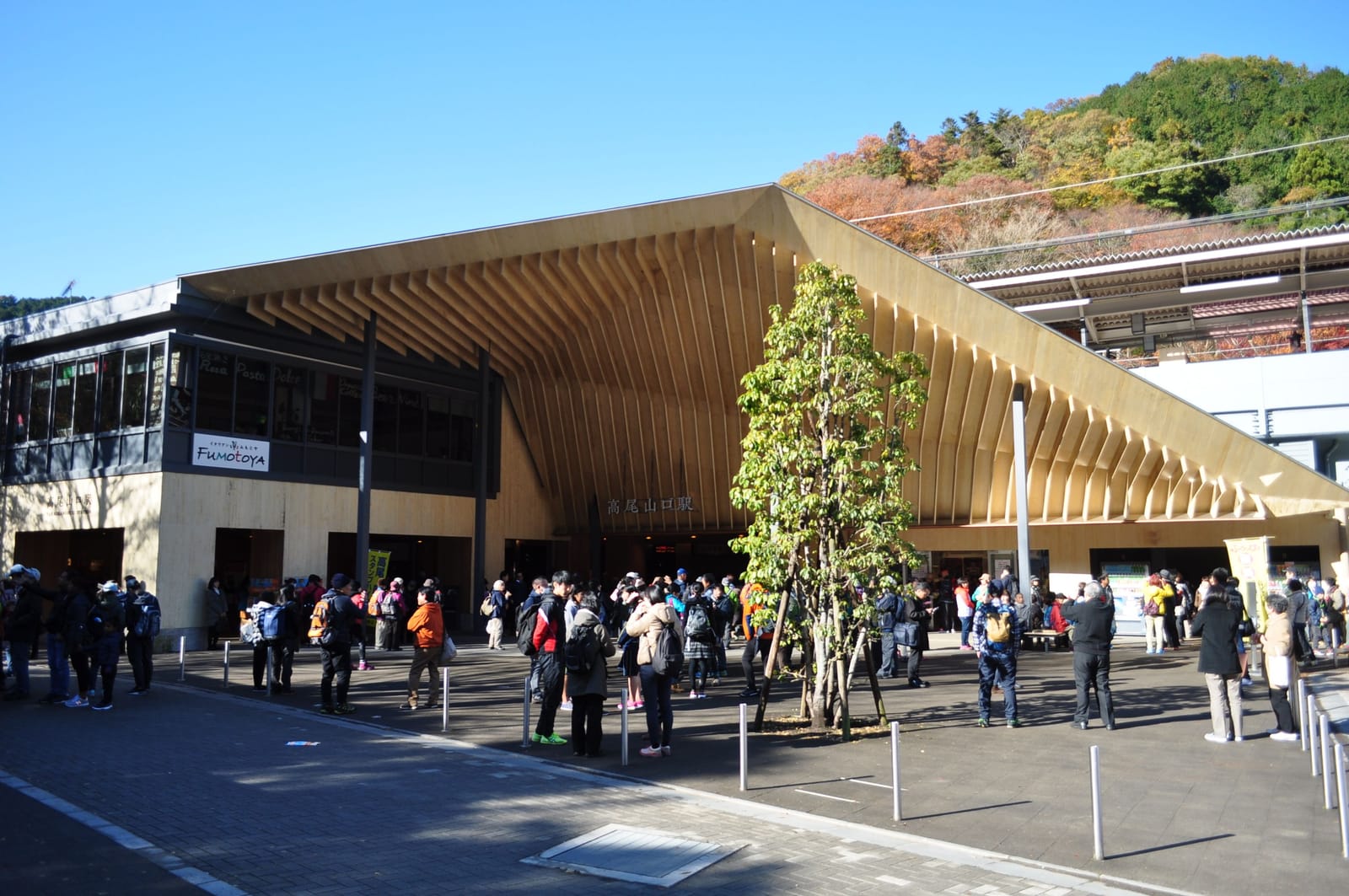 Takaosanguchi Station with its large wooden eaves, and crowds of hikers in the square in front.