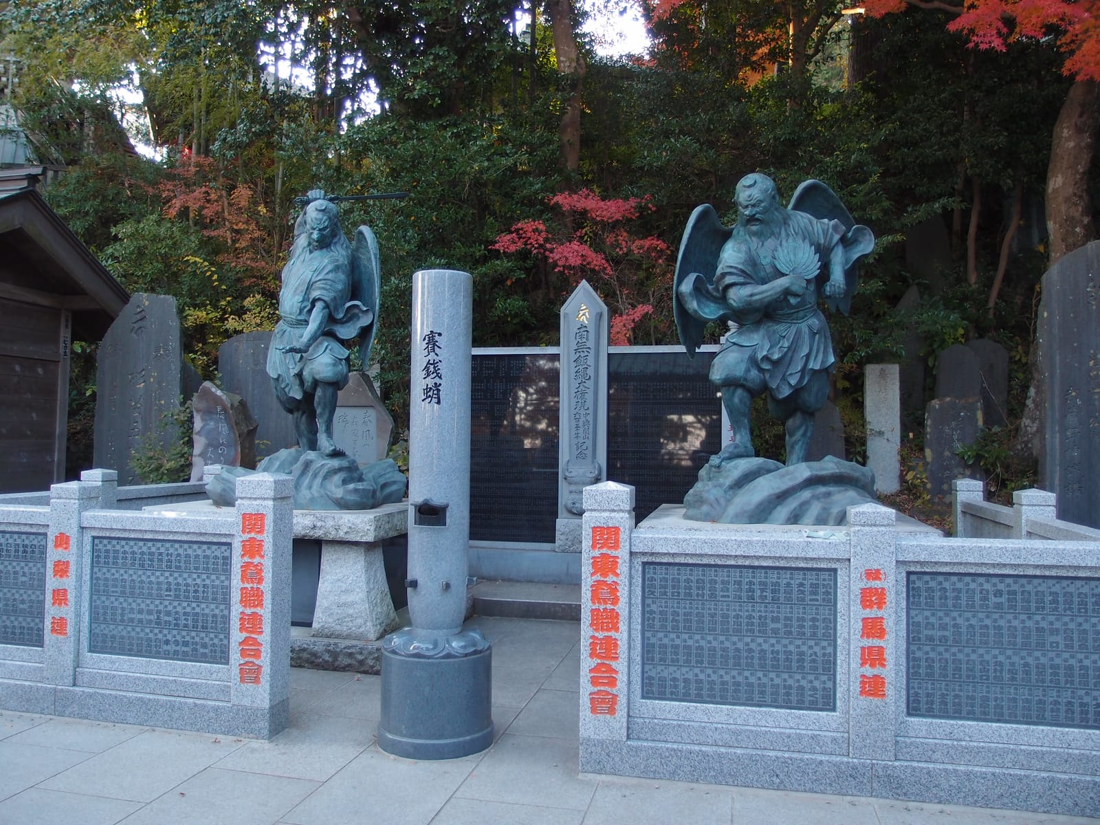 Two bronze winged tengu statues standing on rocks in the grounds of Yakuoin Temple.